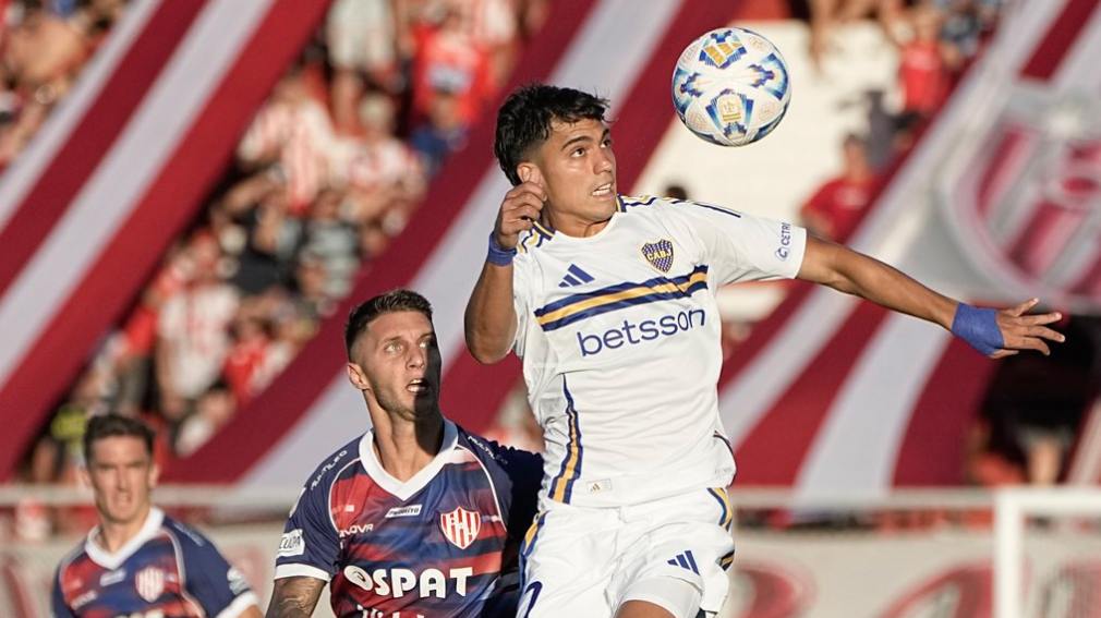 Jugador de Boca y otro de Unión de Santa Fe durante un partido recibiendo una pelota de fútbol.