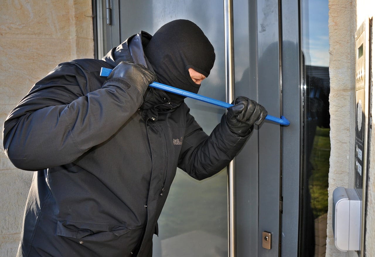 Un ladron vestido de negro tratando de entrar en una casa.